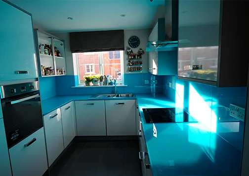 Glass worktop edge profile detail showing the polished edge of toughened back-painted glass with the colour depth visible through the glass cross-section and the chamfered arris that reduces chip risk on exposed corners