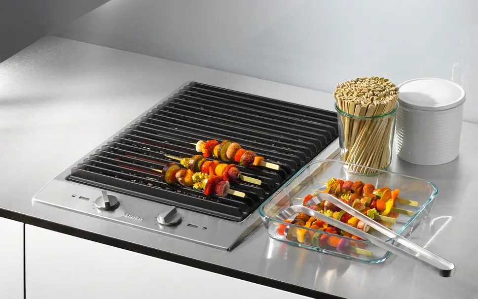 Grill hob domino module installed in a kitchen worktop showing the ridged grate surface with food grill marks and the surrounding stone surface