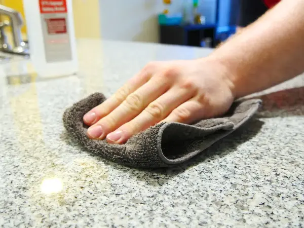 Granite worktop being cleaned with a soft cloth showing the correct daily maintenance approach for polished granite surfaces in a kitchen environment