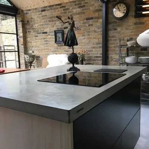 Concrete worktop showing the polished surface with visible aggregate texture and the characteristic tonal variation of cast concrete in a warm grey tone on a kitchen island
