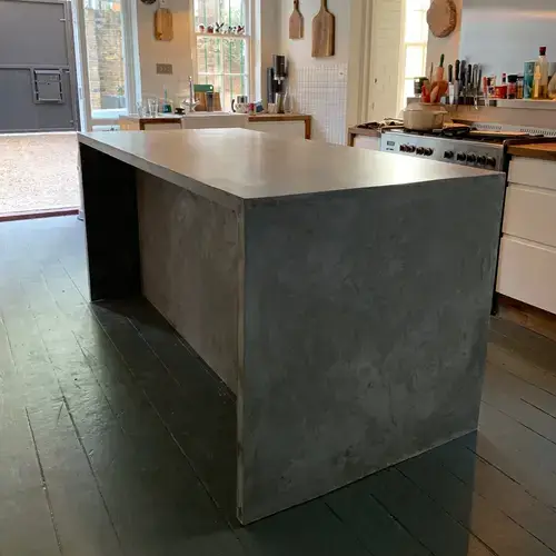 Concrete worktop with a honed matte finish showing the smooth surface and consistent grey tone with subtle aggregate texture visible in the light across a kitchen worktop run in a contemporary design setting