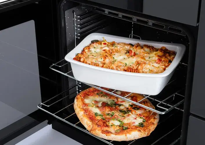 Fan cooking and multi-level cooking in a built-in oven showing multiple trays of food cooking simultaneously on different shelf levels with even heat distribution from the rear fan and heating element circulating hot air throughout the cavity