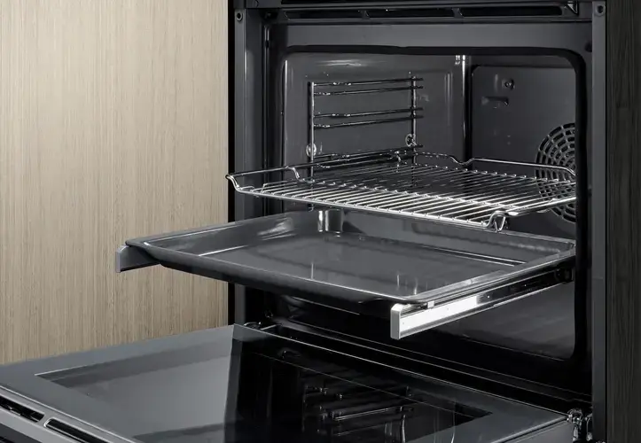 Telescopic rails and soft-close door on a built-in oven showing the fully extended sliding shelf runners that allow a baking tray or roasting tin to be pulled completely out of the oven cavity to a stable position for checking basting or lifting without the tray tipping