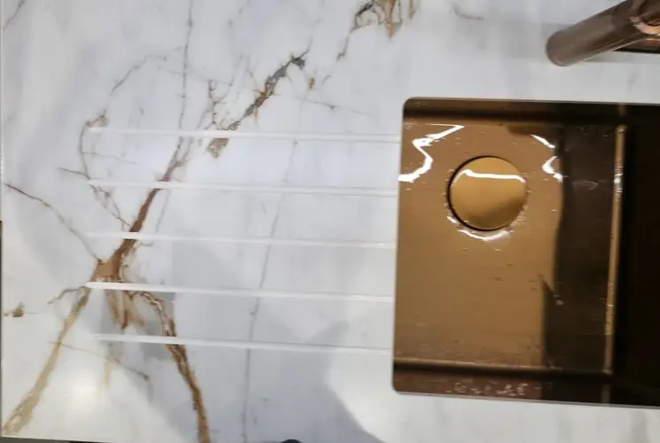 Porcelain worktop with machined drainer grooves showing the plain base material exposed in the groove channels against the patterned surface of the standard surface-print porcelain slab beside the sink