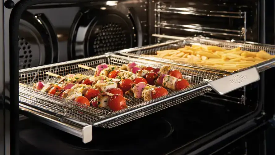 Air fry function in a built-in oven showing the dedicated perforated enamel air fry tray with food being crisped by strong circulating hot air in the oven cavity producing results comparable to a countertop air fryer