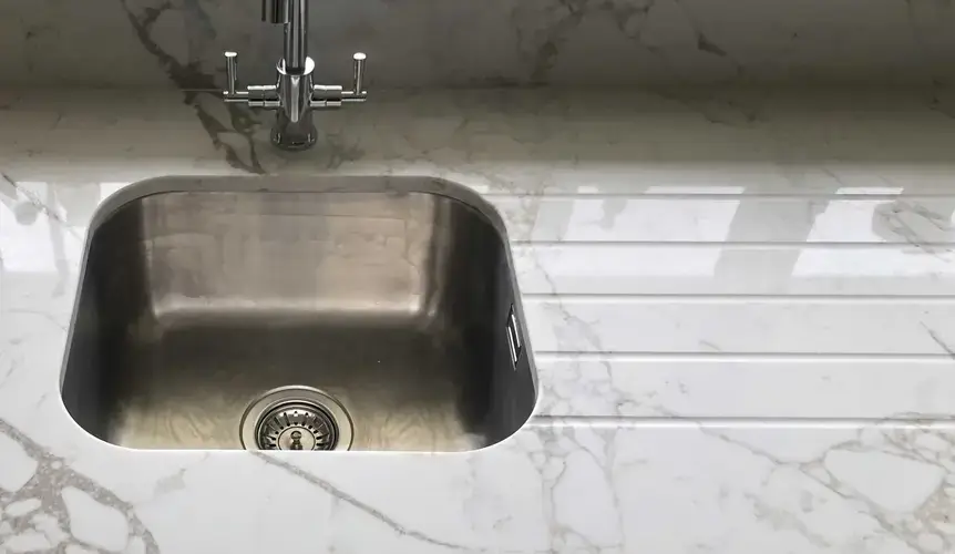Quartz worktop with machined drainer grooves showing the parallel channels cut into the quartz surface beside the sink bowl directing water back into the sink with the grooves running at a slight slope toward the sink bowl