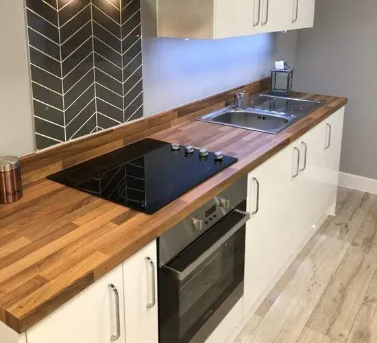 Premium solid wood kitchen worktop showing the butcher block construction and rich natural grain on a large island in a modern kitchen design with integrated appliances