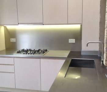 Stainless steel worktop around a hob showing the continuous fabricated surface with no joints between the worktop and the hob surround in a contemporary German kitchen design with the characteristic brushed finish